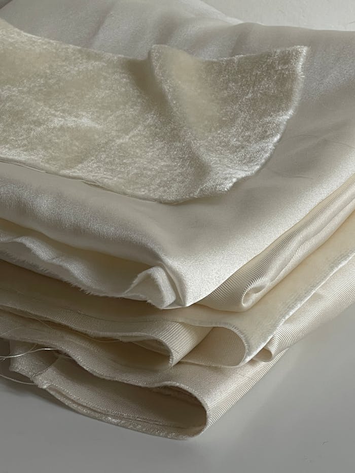 Close-up view of elegant ivory silk and velvet fabrics folded neatly in a stack, showcasing their delicate and soft texture.