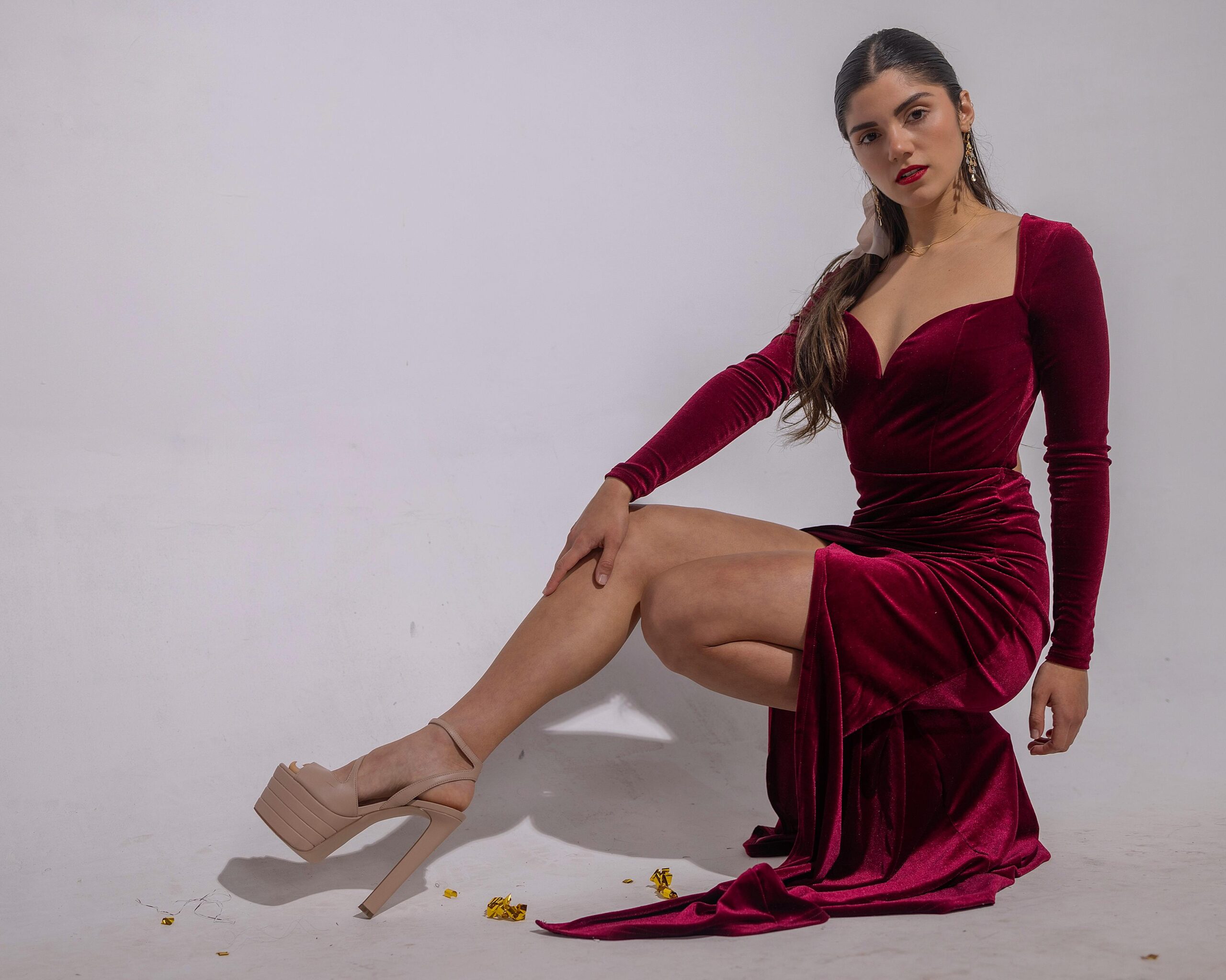 Sophisticated portrait of a woman in a red dress posing on a studio white background.